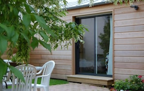 A patio area with a table and chairs, a sliding glass door, and a wooden exterior wall. - Couette et Cafe creme (Le Coudray)