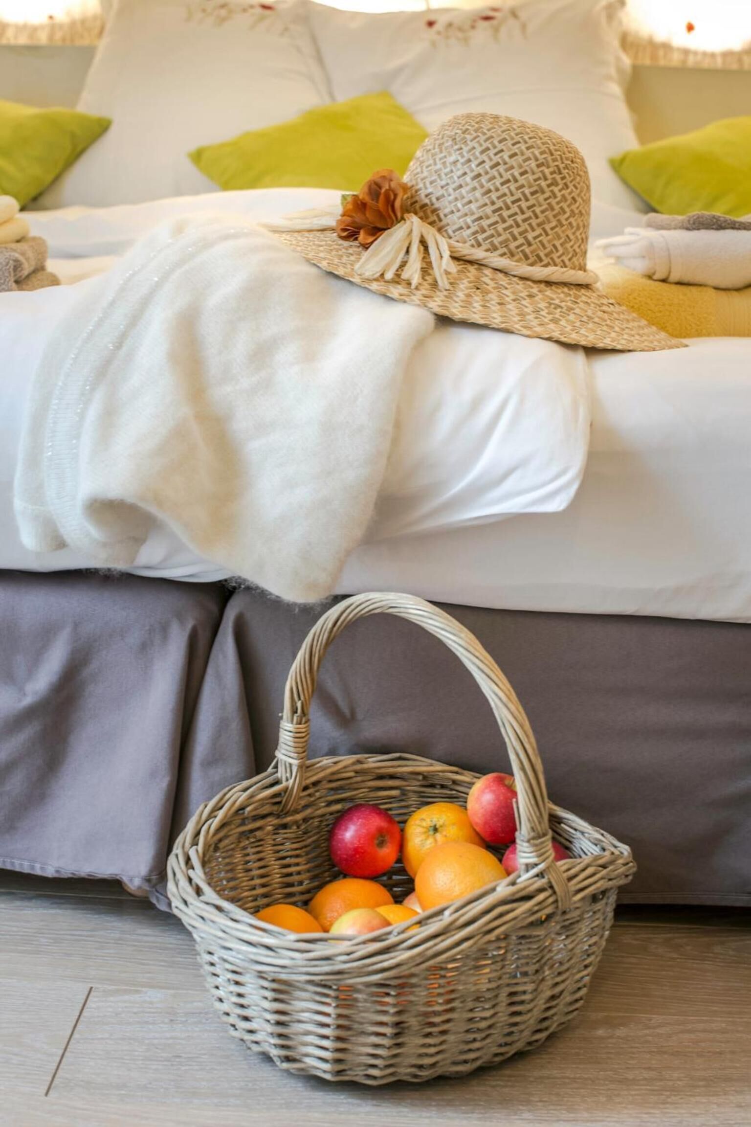 Ein Bett mit weißer Decke und einem Korbwägelchen voller Früchte auf Holzboden.