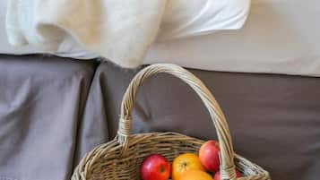 Ein Bett mit weißer Decke und einem Korbwägelchen voller Früchte auf Holzboden.