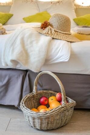 A bed with a white blanket and a wicker basket filled with fruits on a wooden floor. - Couette et Cafe creme (Le Coudray)