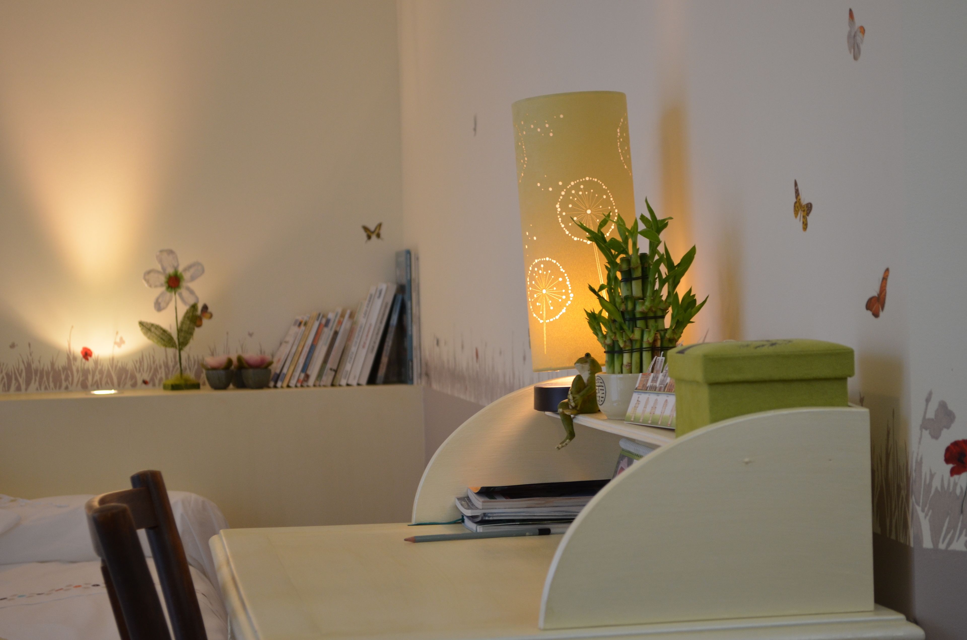 Un dormitorio con una cama, un escritorio con silla, una lámpara y adornos en la pared con mariposas y flores.