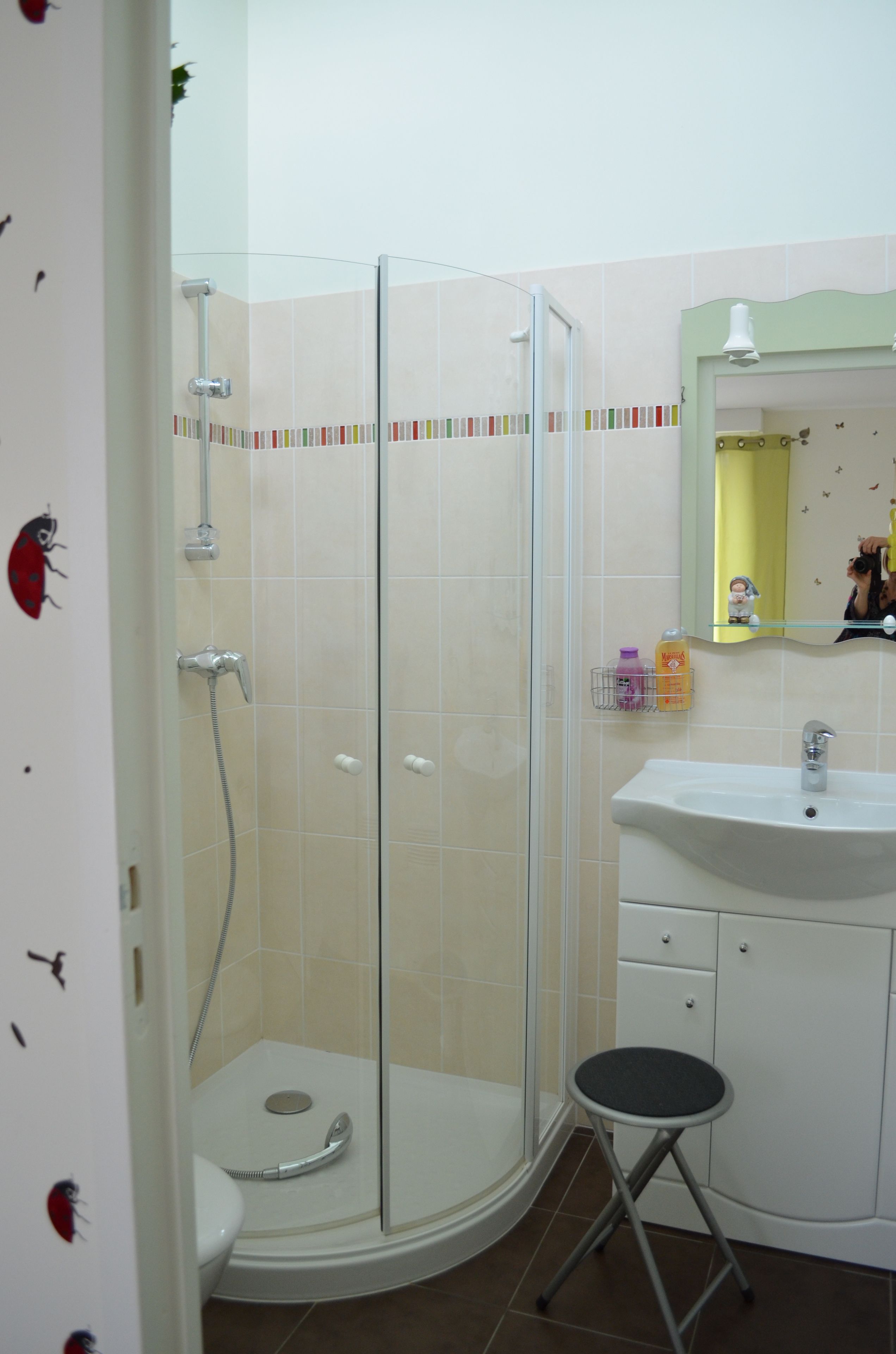 Une salle de bain avec une douche à parois de verre, un lavabo blanc et un petit tabouret.