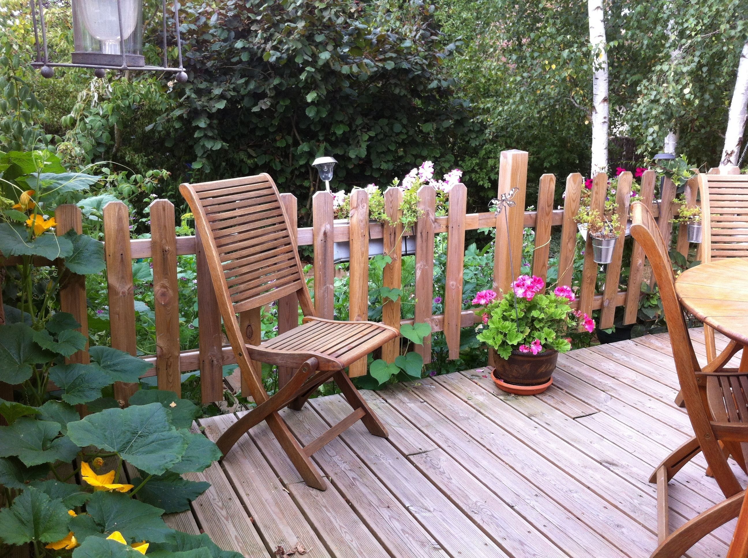 A wooden deck with a wooden chair and a table, surrounded by a wooden fence and potted plants.