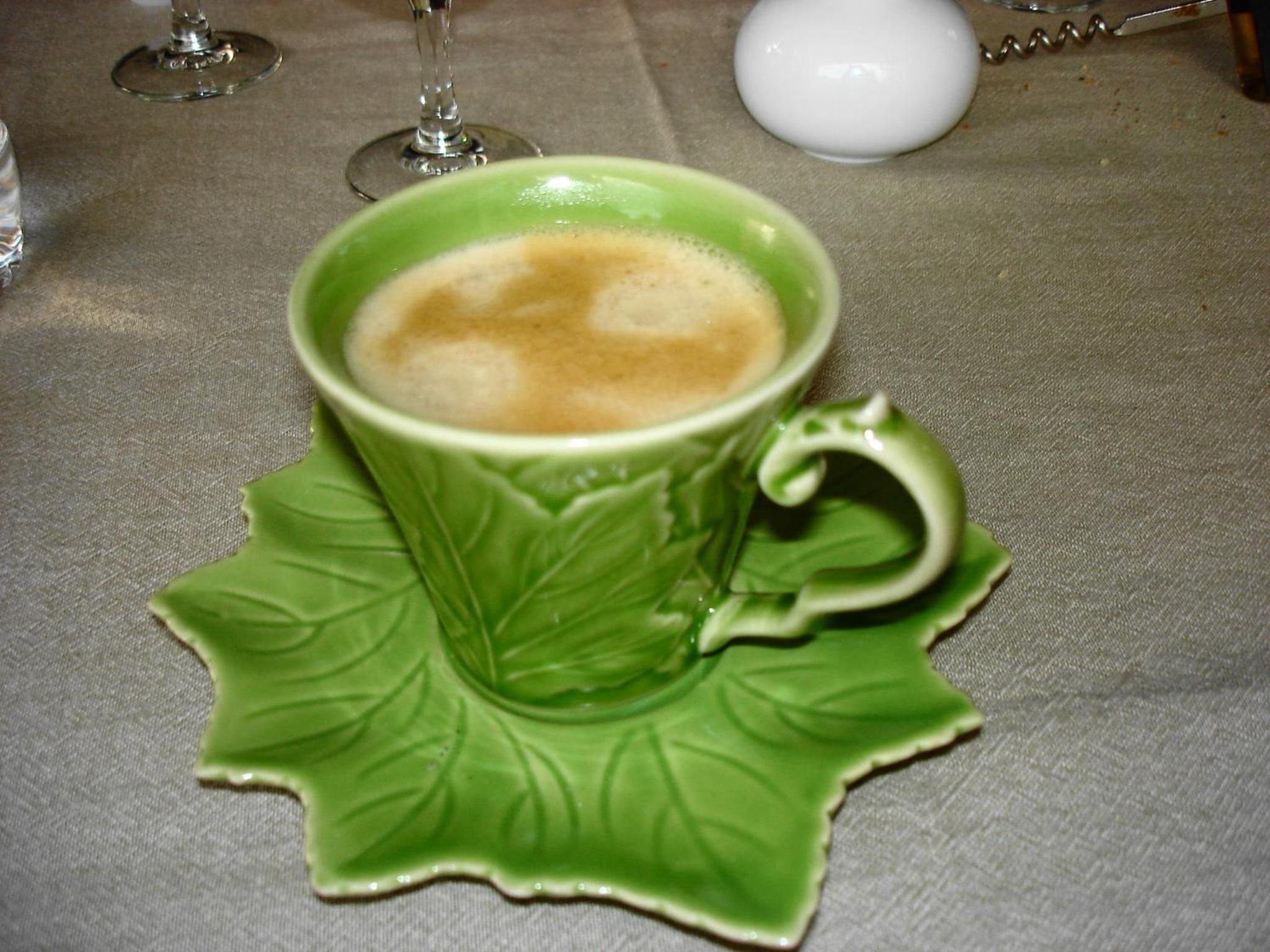 Una taza de café sobre un platito verde con diseño de hoja.