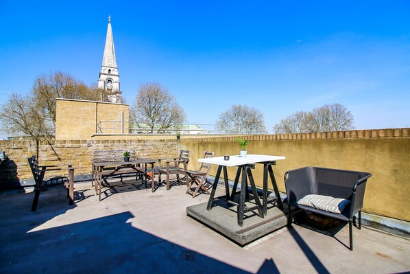 Eine Terrasse im Freien mit Tischen und Stühlen, einem kleinen Blumentopf und im Hintergrund einem Blick auf den Kirchturm.