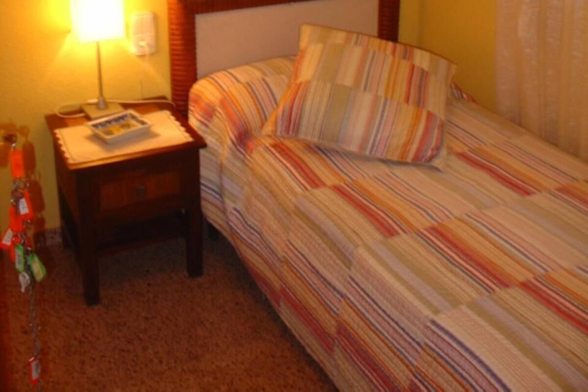 A single bed with a striped bedspread in a room with yellow walls and a wooden headboard.