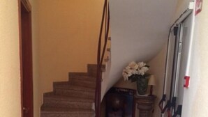 En smal hall med en matta som täcker trappan, vilken leder upp till en liten plattform. På plattformen står en stol och en vas med blommor.
