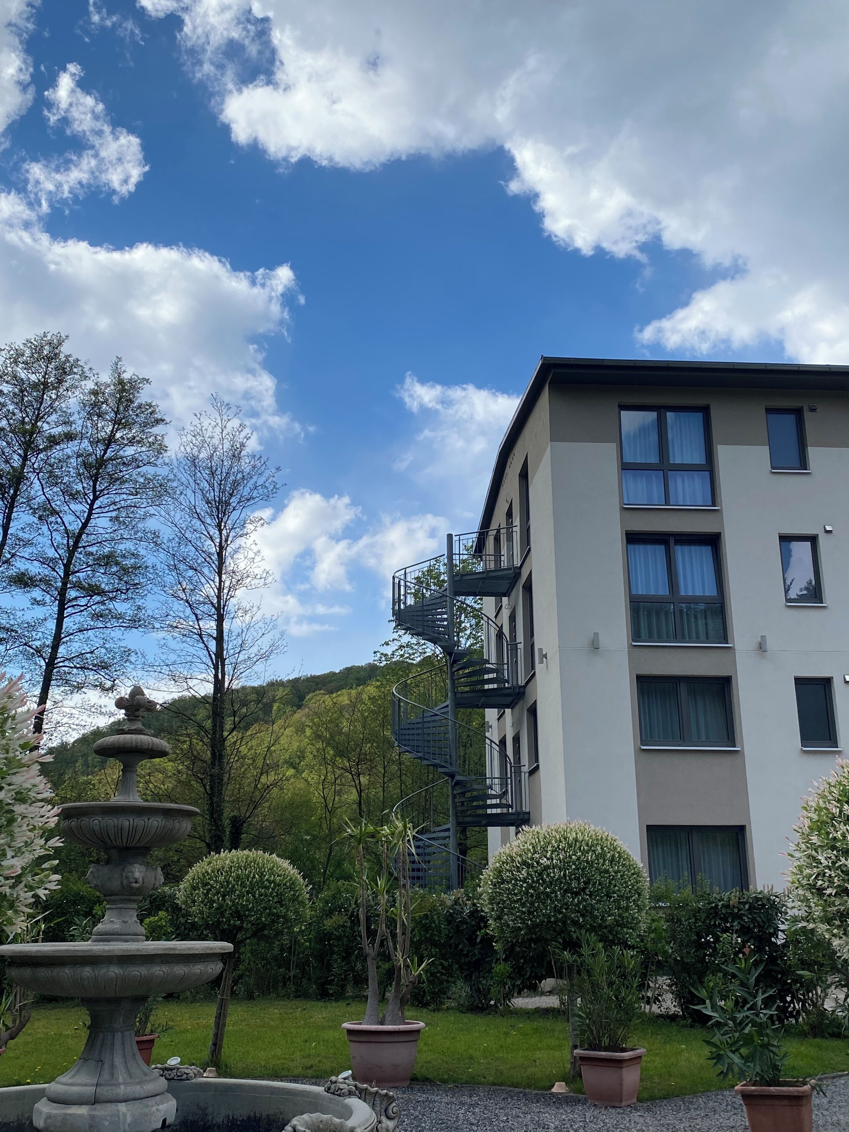 A modern building with a spiral staircase, surrounded by well-maintained gardens and trees.