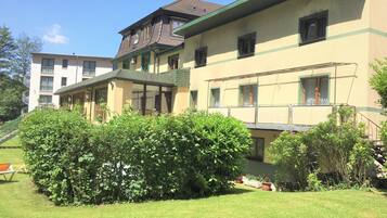 A multi-story building with a green roof and multiple windows. There is a well-maintained lawn in the foreground with a bench.