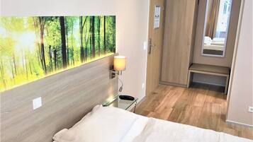 Una habitación de hotel con una cama, una lámpara de pared, un armario y un espejo.