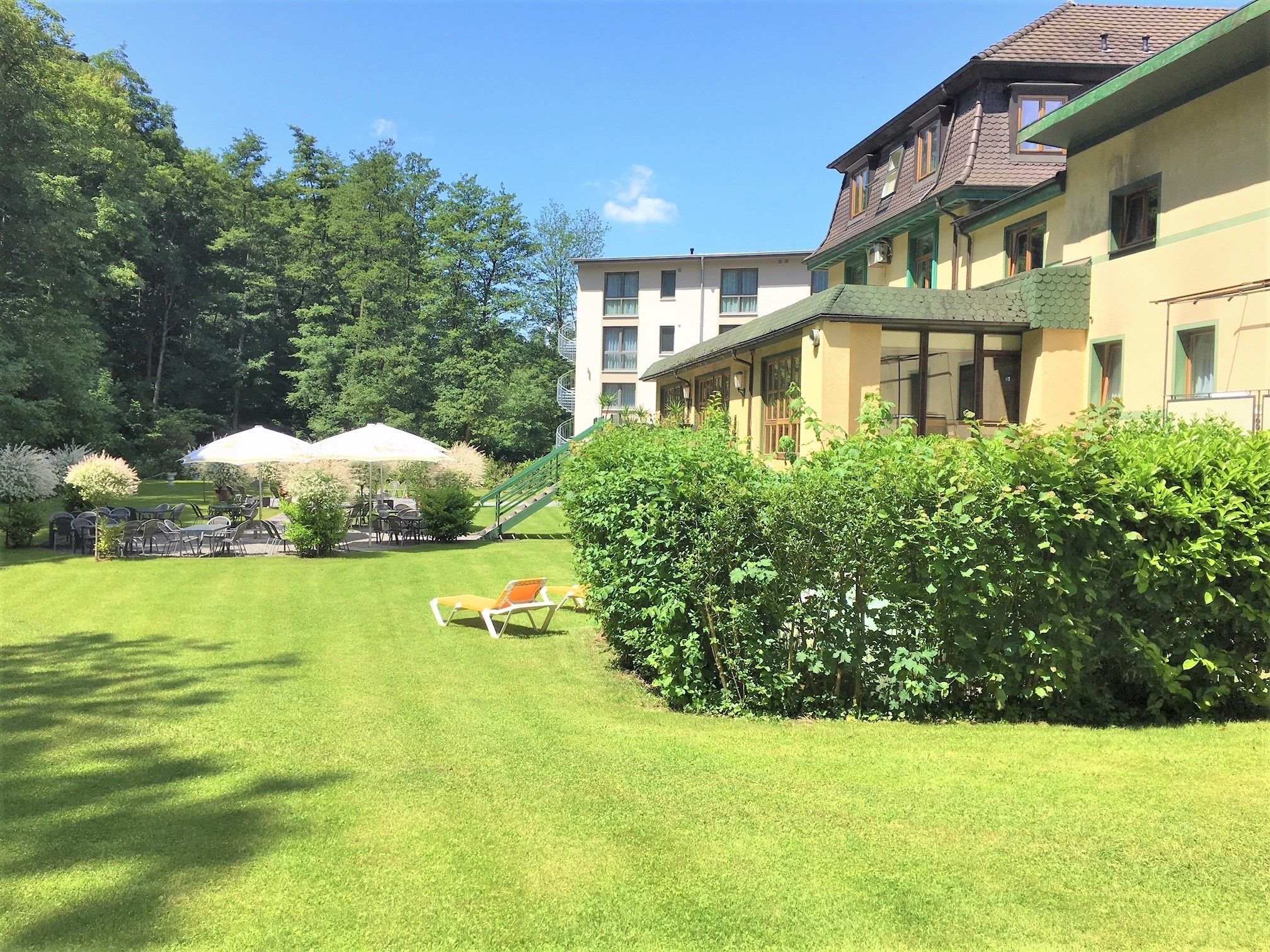 A hotel courtyard with a grassy lawn, outdoor seating, and a staircase leading to the building.