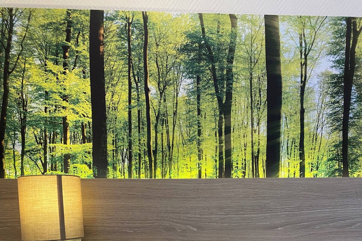 Un dormitorio con cama, una mesita de noche con lámpara y un estante en la pared con un jarrón de plantas secas.