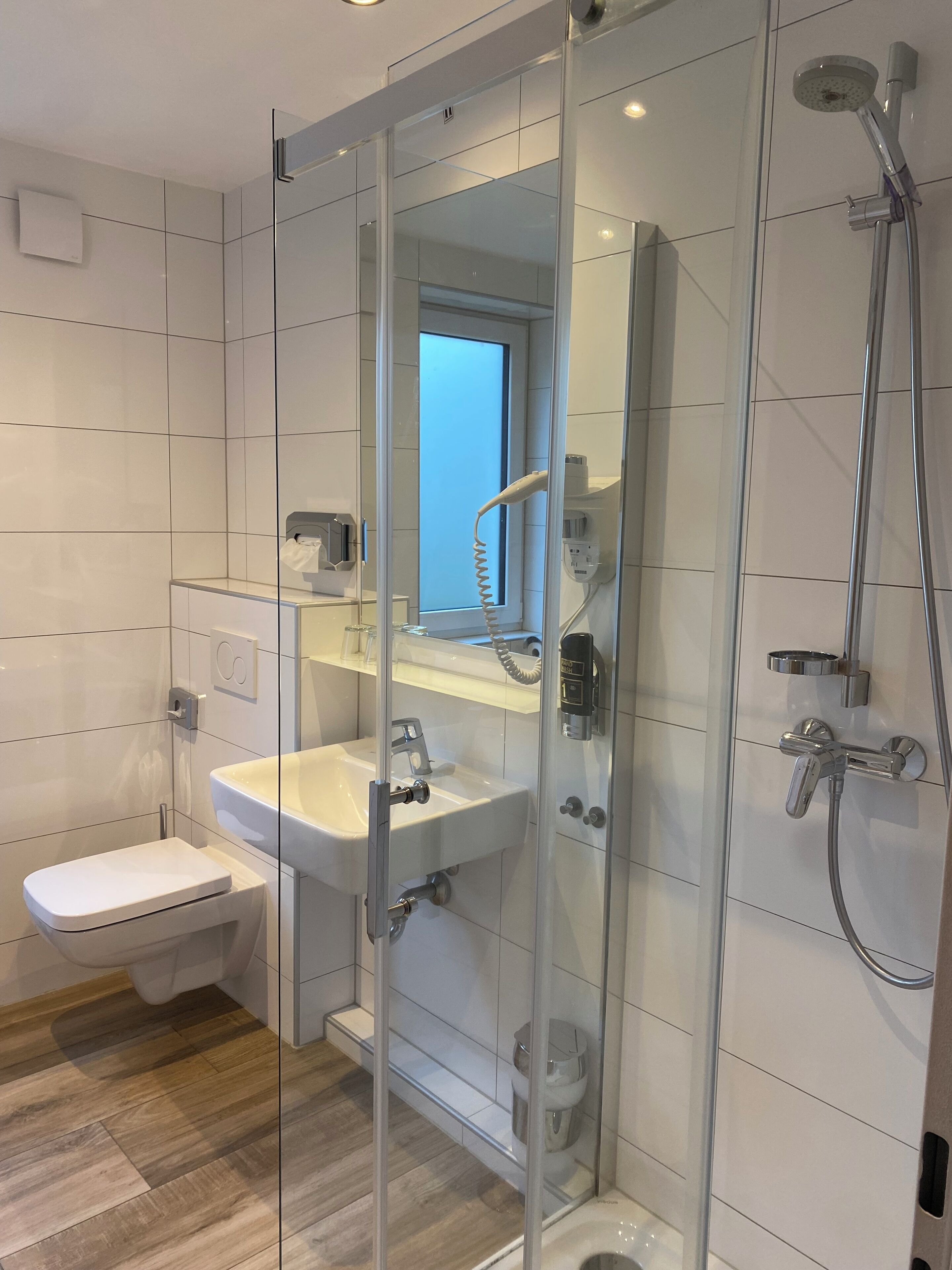 A modern bathroom with a glass-enclosed shower, a white sink, and a toilet.