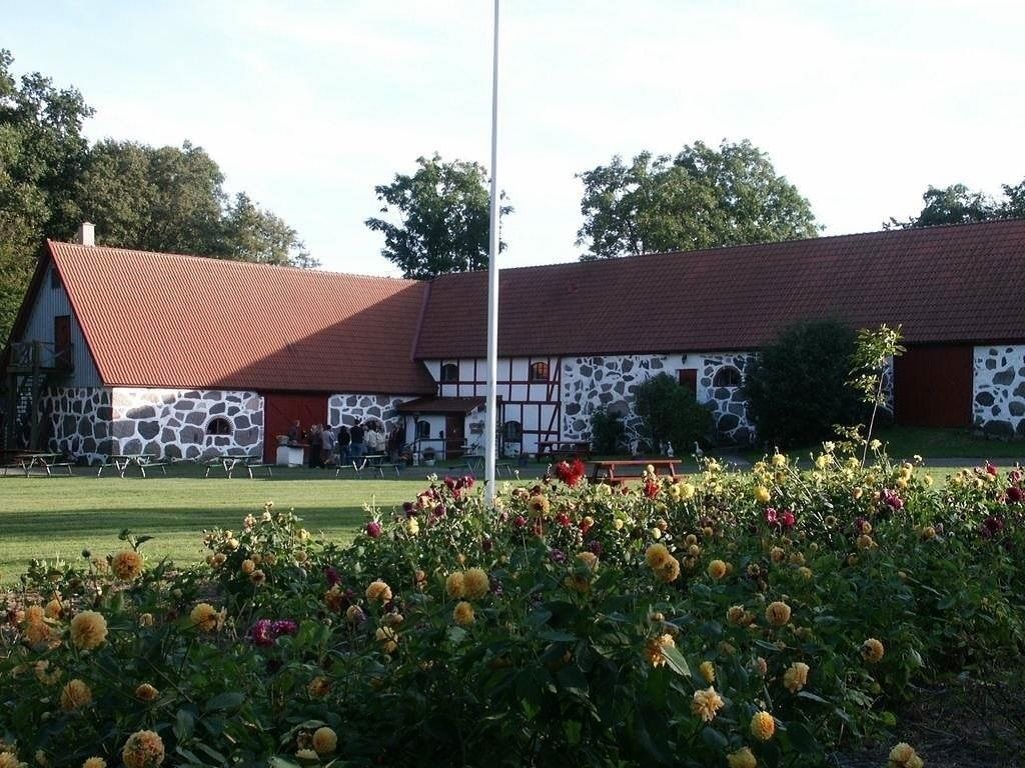 Um edifício com telhado vermelho e paredes de pedra, rodeado por um jardim com flores amarelas.