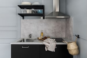 A kitchen with a stainless steel sink, a black shelf with dishes, a bottle, and a woven basket.
