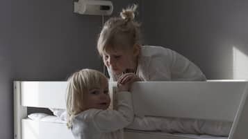 A bunk bed with a child standing on the lower bunk and an adult leaning on the upper bunk.