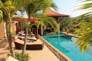 Una piscina con borde de azulejos, rodeada de palmeras y plantas en macetas.
