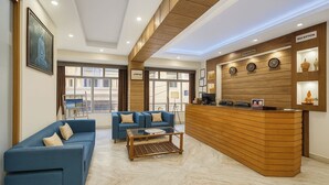 A reception area with a wooden reception desk, two blue sofas, a coffee table, and a large window. - Golden Dolma (Darjeeling)