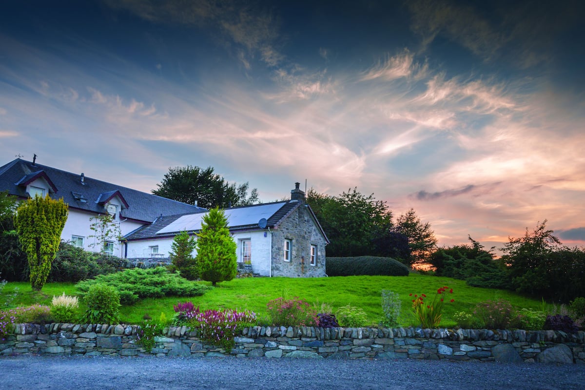 A two-story house with a stone facade, a sloped roof, and a well-maintained garden with various plants and flowers.