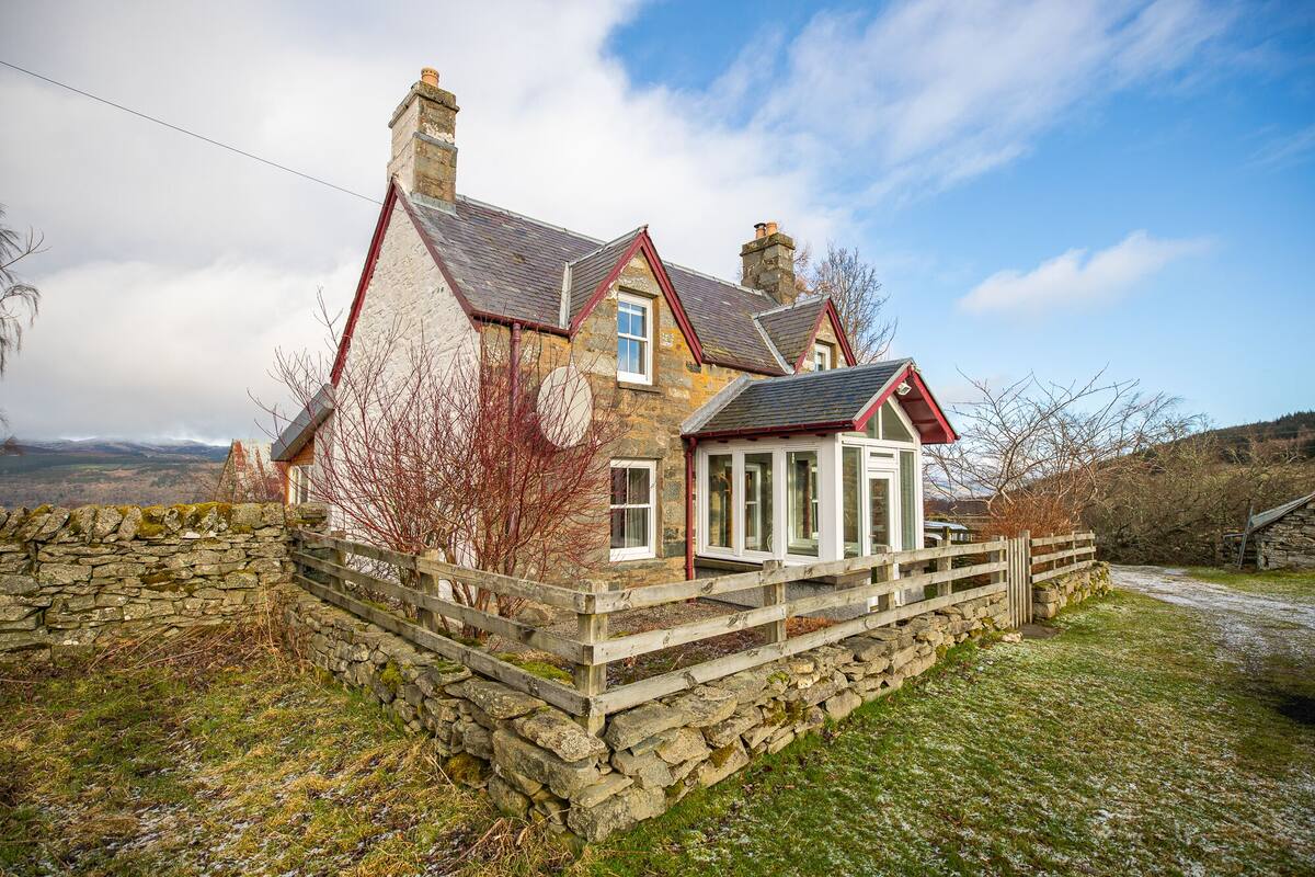 A stone house with a red roof, a stone wall, and a wooden fence.