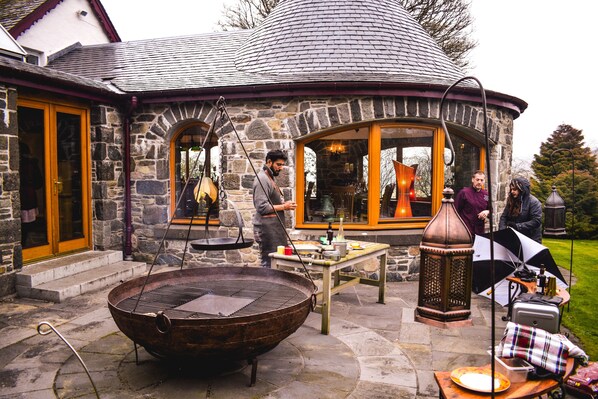 A stone building with a large grill outside, a table with items, and a person standing by the grill.
