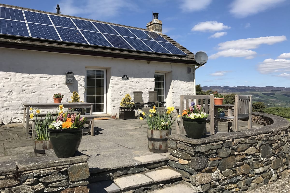 A white stone building with solar panels on the roof, outdoor seating, and potted plants.