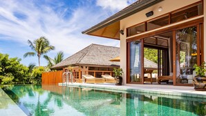 A clear swimming pool with lounge chairs and a wooden deck, surrounded by lush greenery and a modern house with large windows. - Aspire Villas Koh Phangan (Ko Pha-ngan)