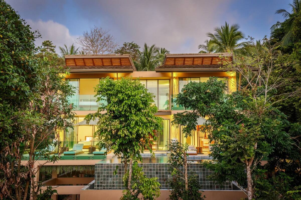 Ein modernes, zweistöckiges Haus mit Glasfassade, Schwimmbad und üppiger, umgebender Bepflanzung.