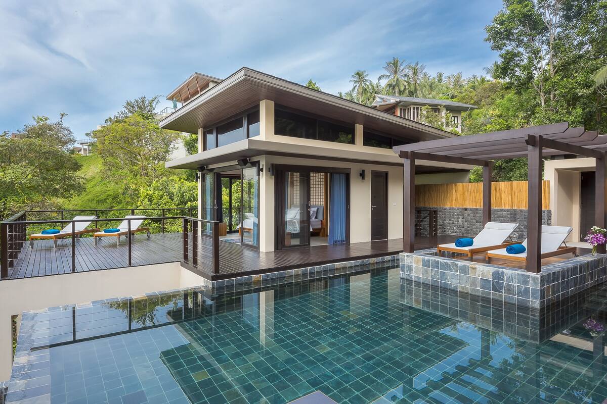 Ein modernes, zweistöckiges Haus mit Swimmingpool, Liegestühlen und Blick auf die umliegende Grünfläche.