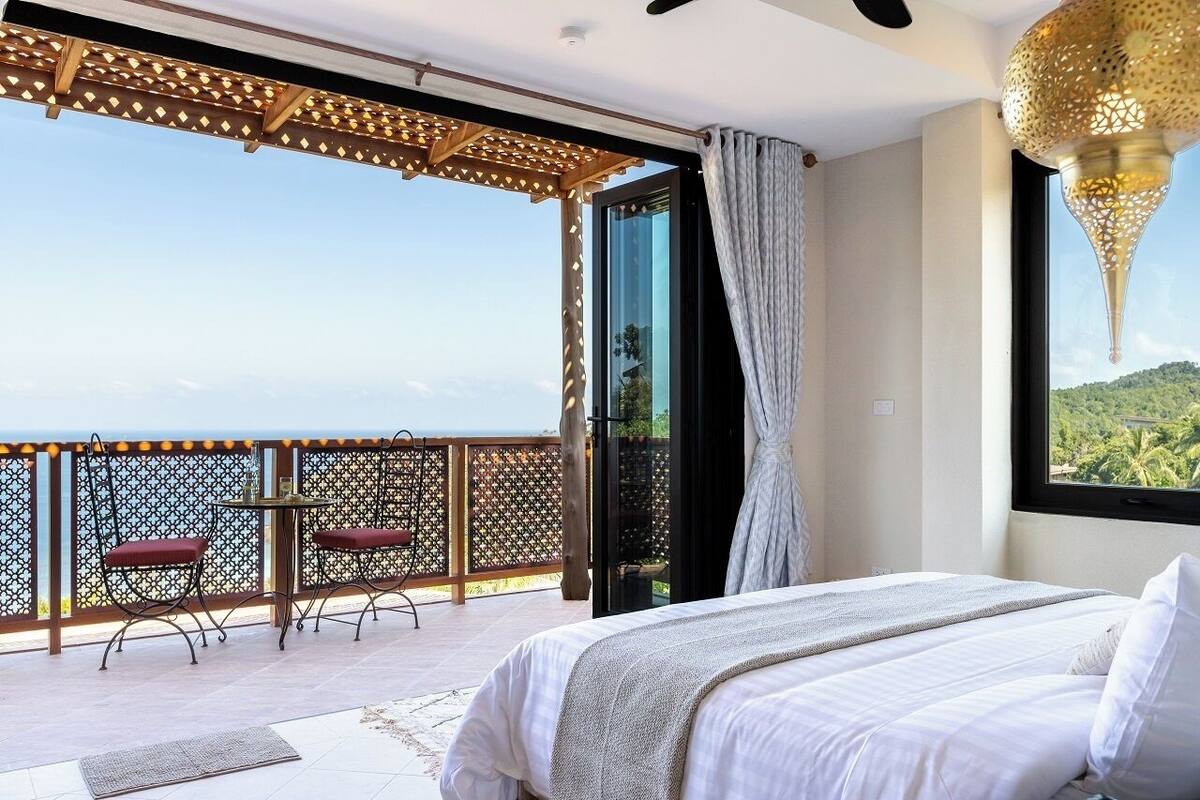 Ein Schlafzimmer mit einem großen Bett, einem Balkon mit Tisch und Stühlen und Blick auf die Landschaft.