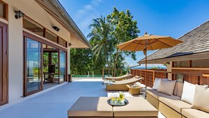 Un espace de détente extérieur moderne, doté d’un patio fermé par des baies vitrées, de sièges confortables et offrant une vue sur des palmiers.