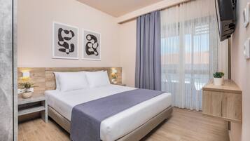 Habitación de hotel moderna con una cama grande, cabecera de madera, mesita de noche con lámpara y una pequeña planta en maceta.