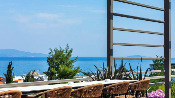 An outdoor seating area with wicker chairs and a table, overlooking a coastal view with the sea and distant mountains. - Hotel Vozina (Polygyros)