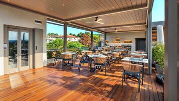 An outdoor dining area with wooden flooring and wicker chairs, overlooking a scenic landscape.