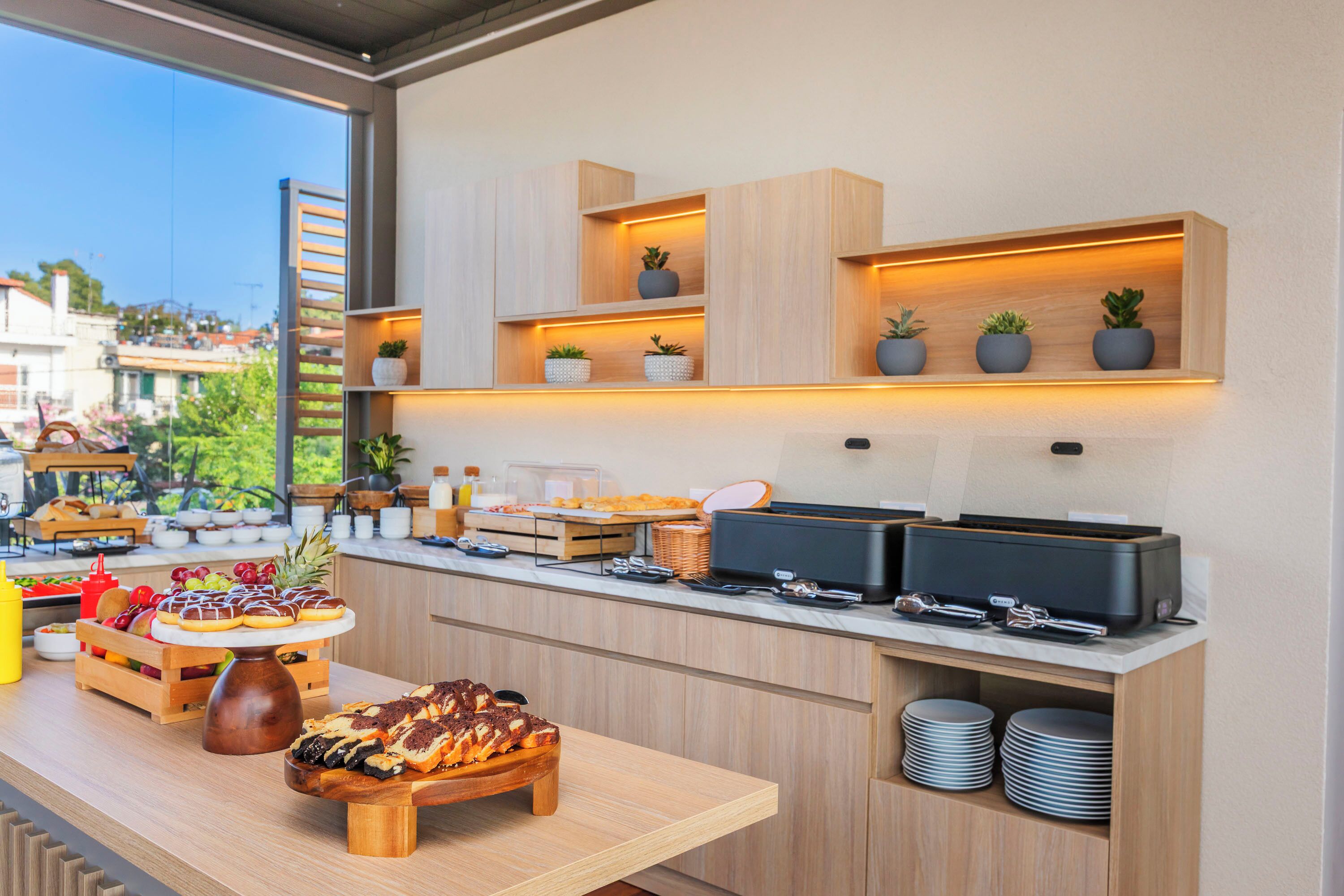 A buffet setup with various food items, a coffee machine, and potted plants on shelves.