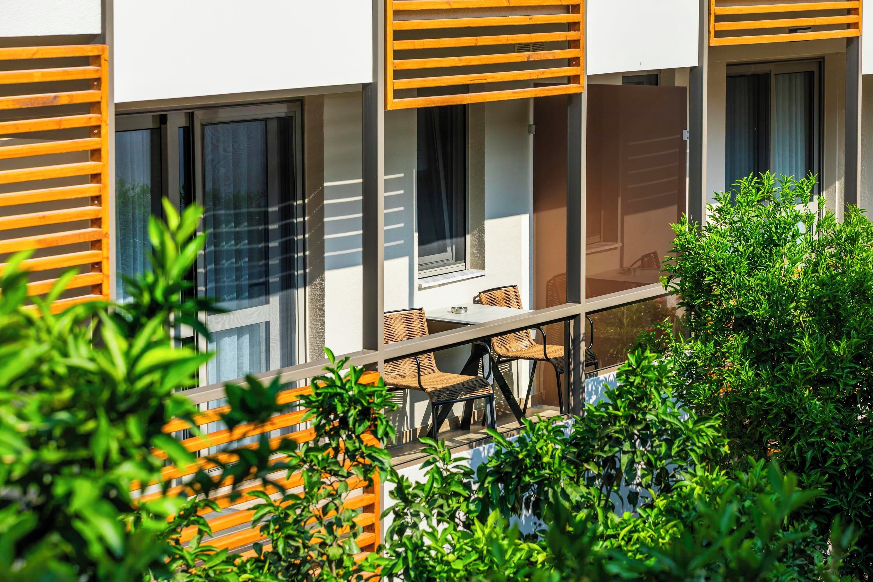 A modern building with a balcony, outdoor seating, and greenery.