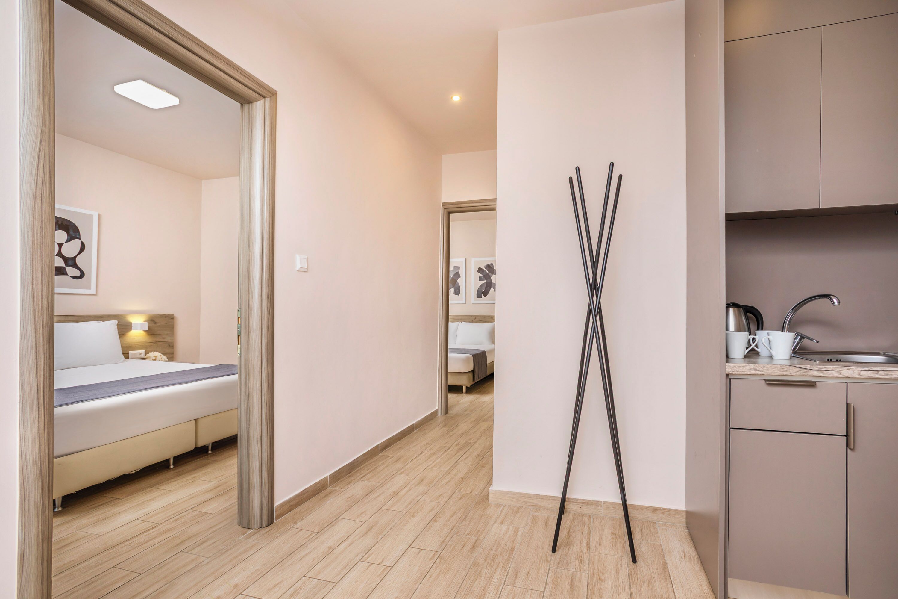 A modern hotel room with a bed, bedside table, and a view into the adjacent room.