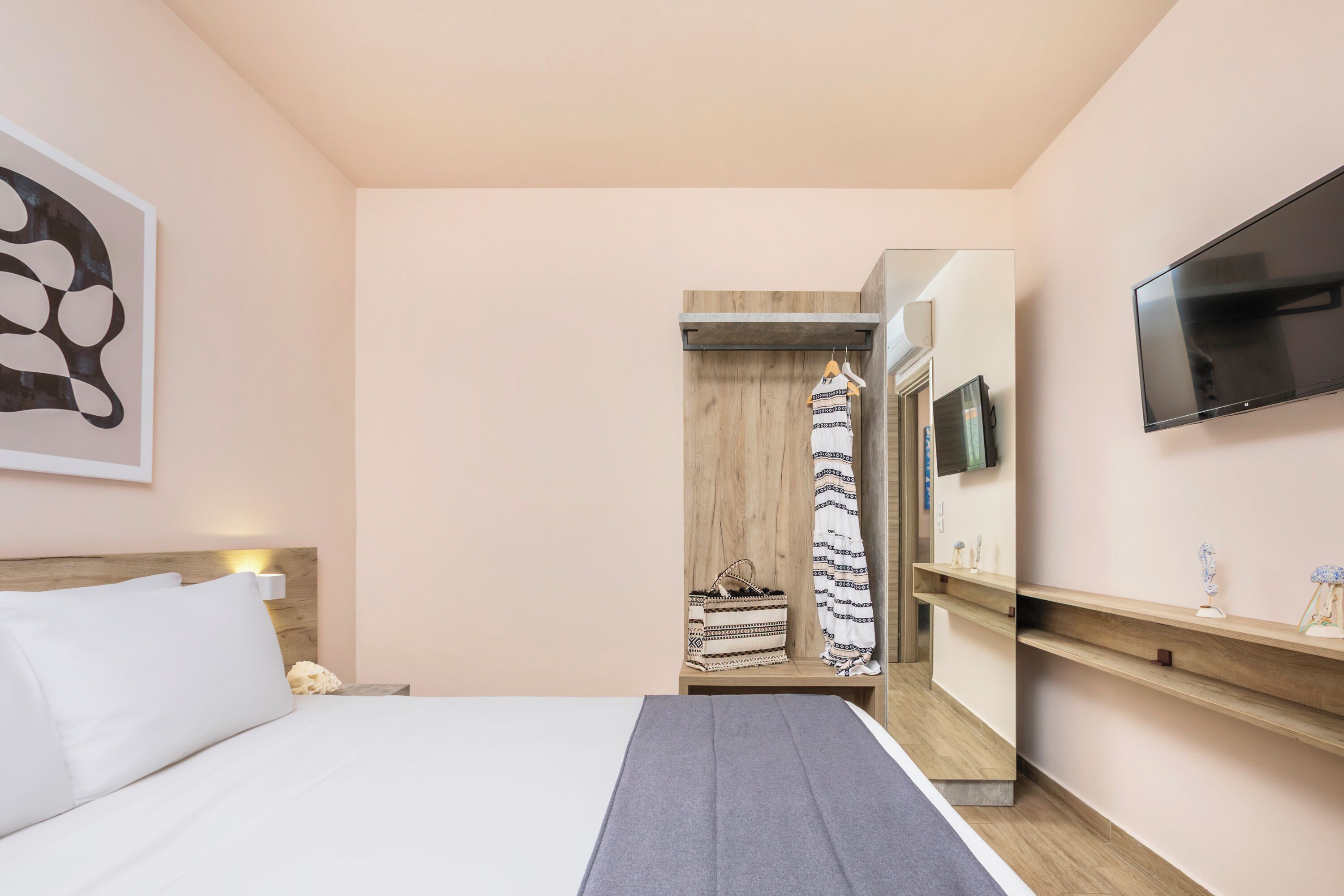 Ein Hotelzimmer mit einem Bett, einem an der Wand montierten Fernseher, einem Holzschrank und einem Spiegel.