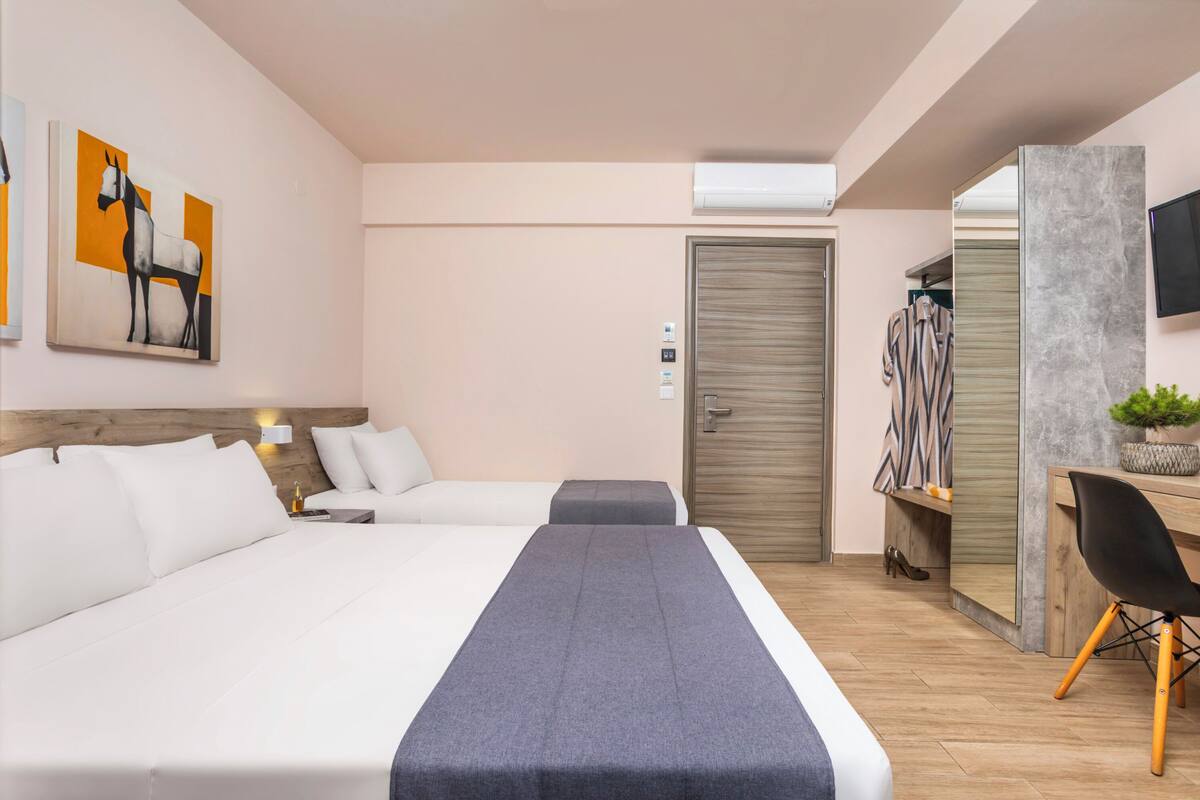 A modern hotel room with a large bed, a desk, a chair, and a wardrobe.