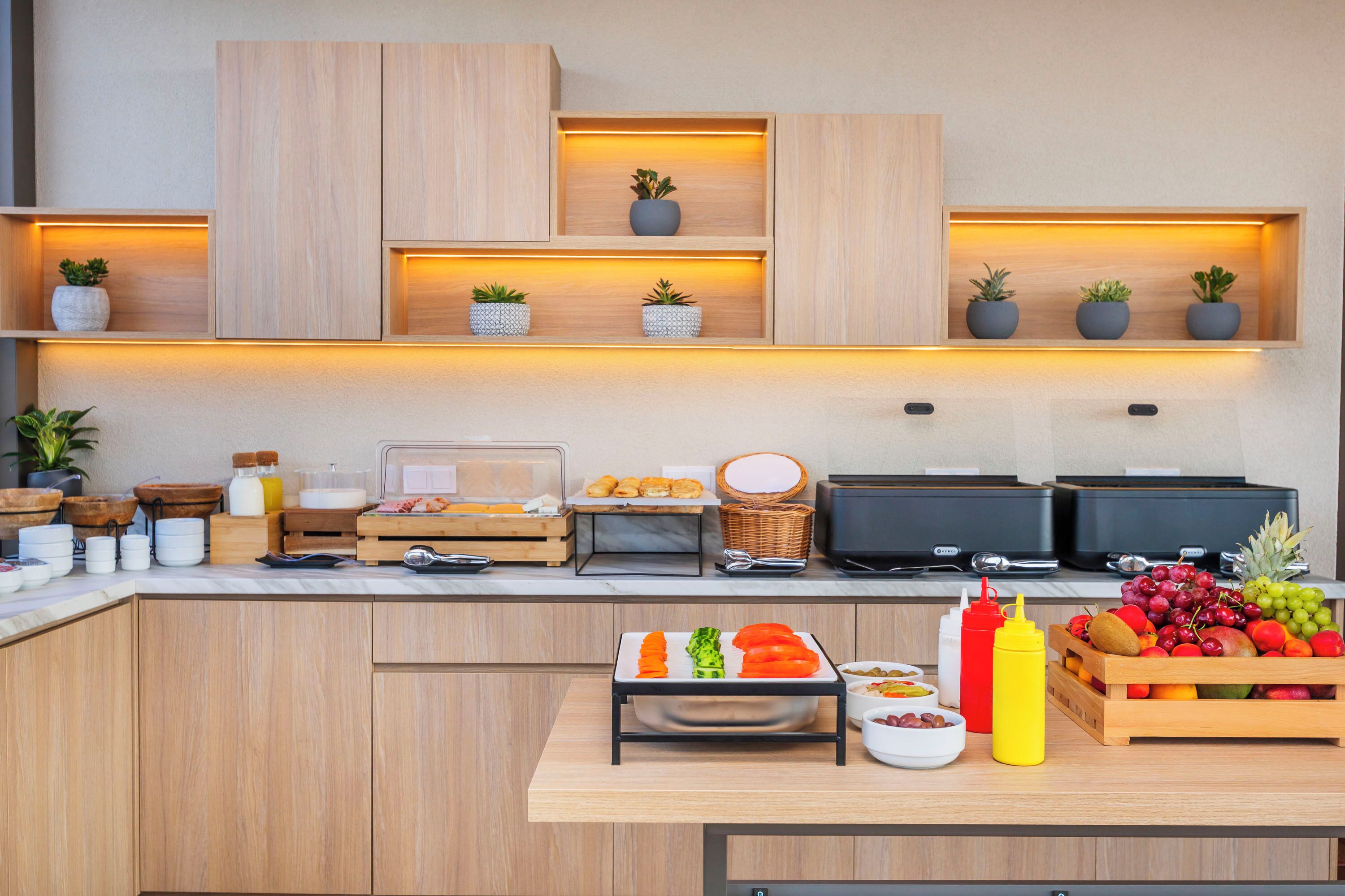 A modern kitchen with wooden cabinets, built-in shelves with potted plants, a fruit display, and a breakfast bar.