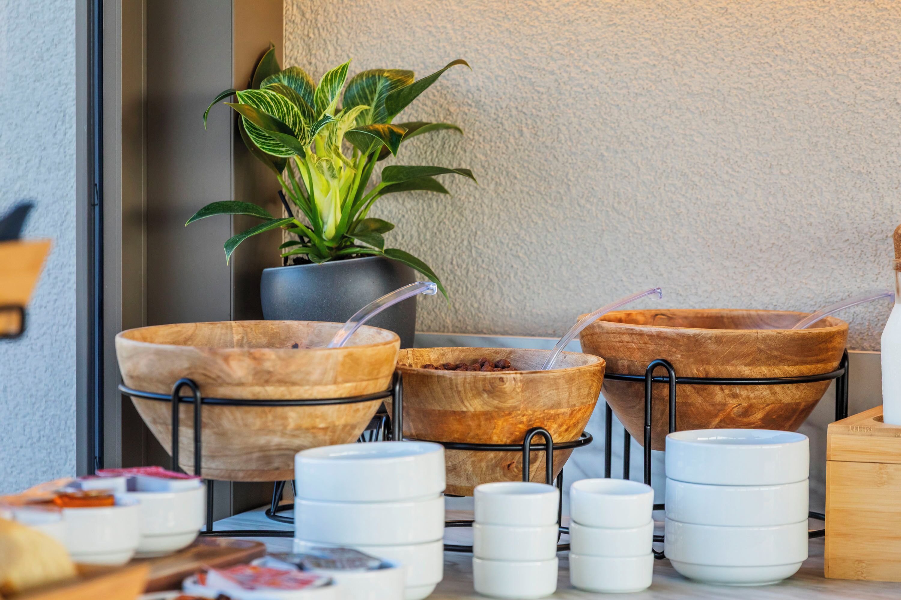 A table with wooden bowls and white mugs, a potted plant, and a wooden box.
