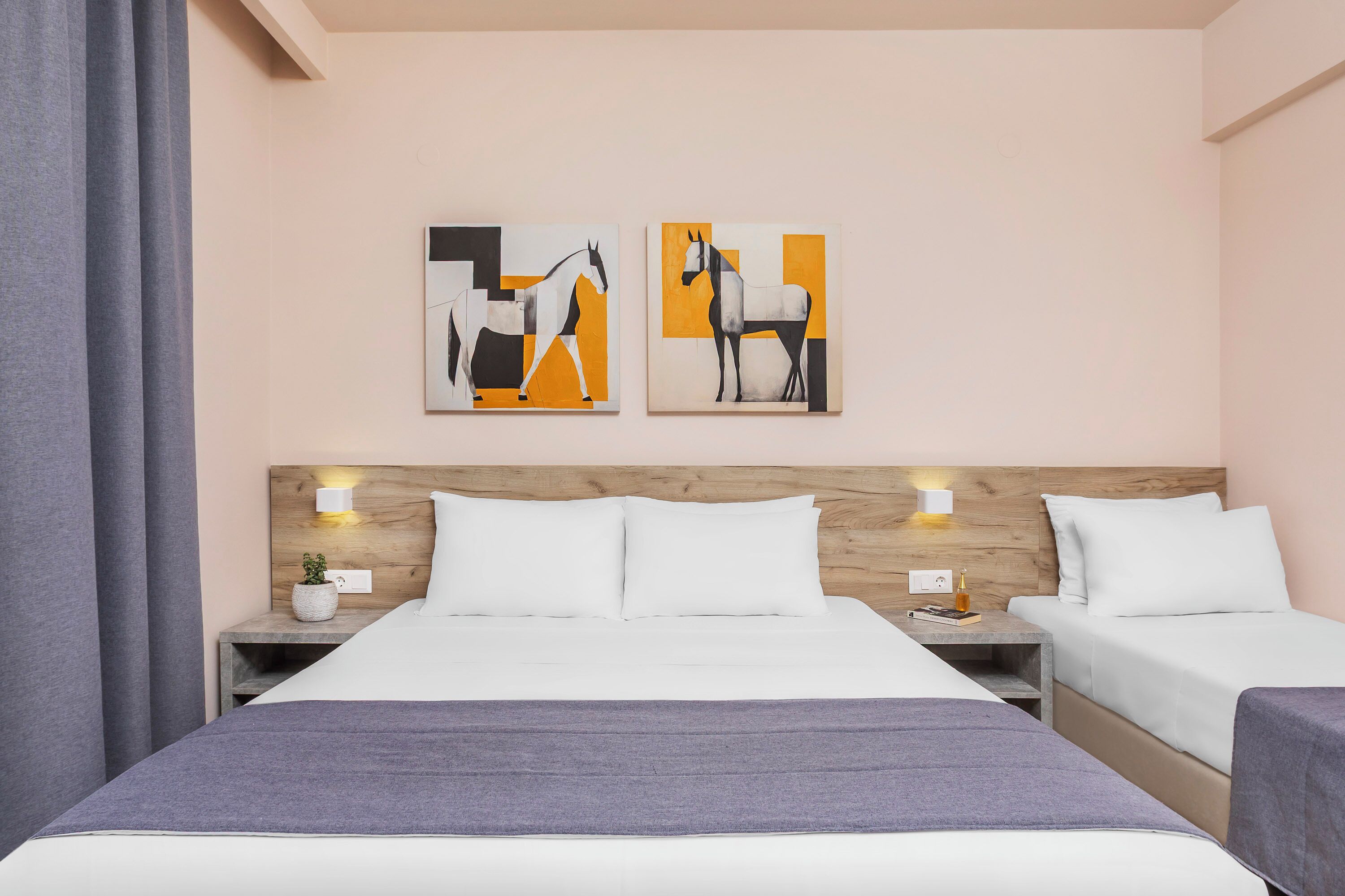 A hotel room with a wooden headboard, two beds, a nightstand with a lamp, and two abstract paintings on the wall.