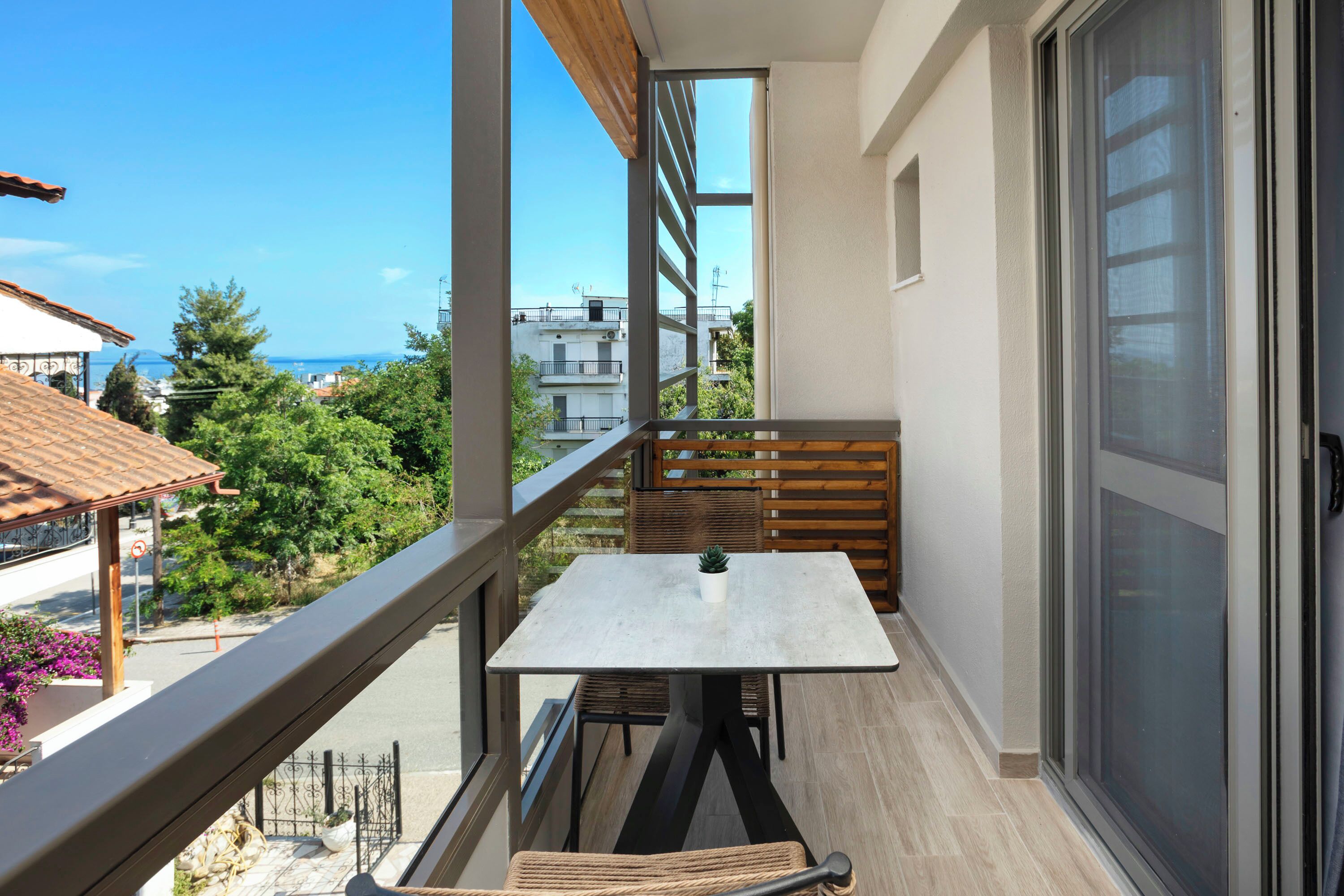 En balkong med ett bord och stolar, med utsikt över ett bostadsområde och havet.