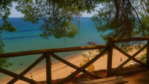 A wooden deck overlooking a beach with a lifeguard tower and beach umbrellas. - Hotel Vozina (Polygyros)