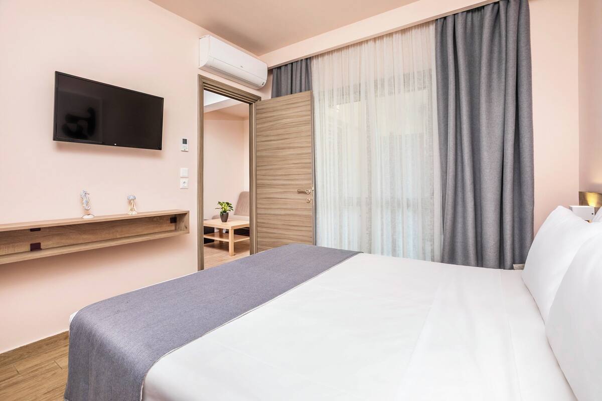 A hotel room with a bed, a TV mounted on the wall, a desk with a chair, and a window with curtains.