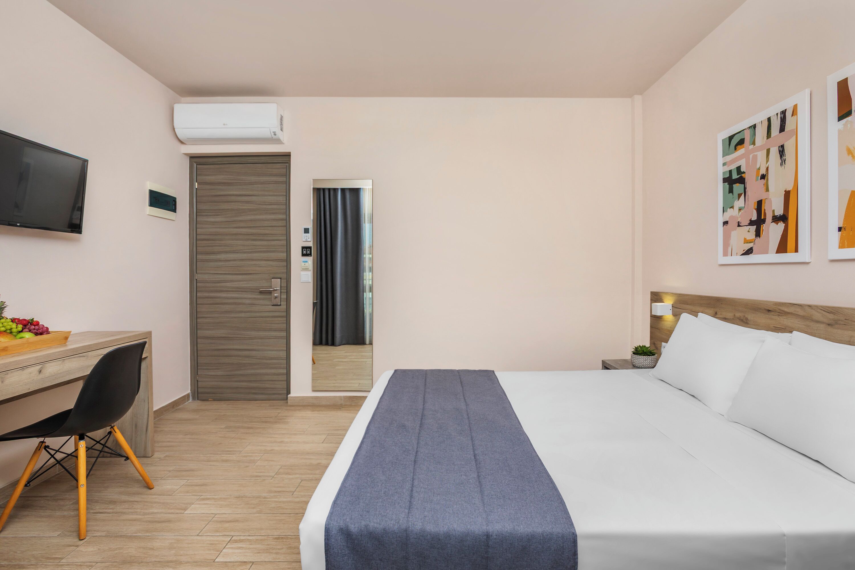 A hotel room with a bed, a desk with a chair, a TV, and artwork on the wall.