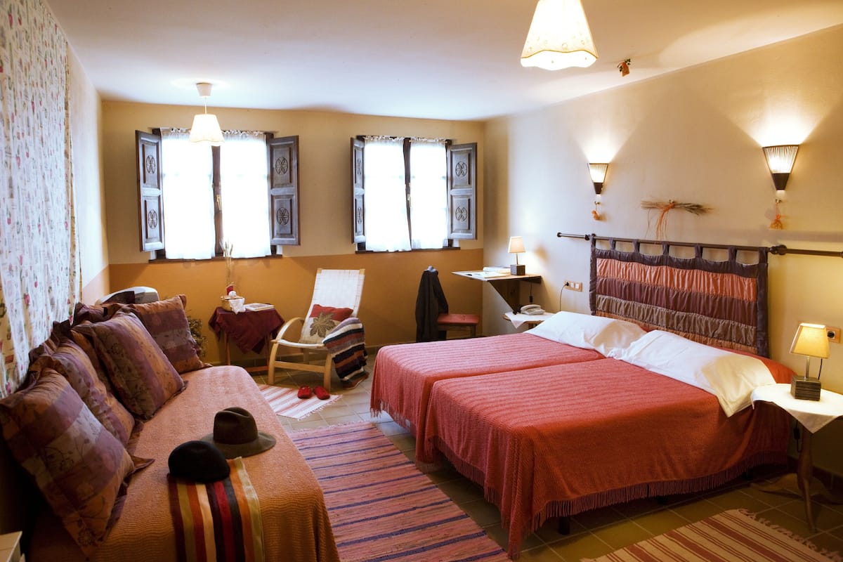 A hotel room with two beds, a sofa, a chair, a small table, and a lamp.