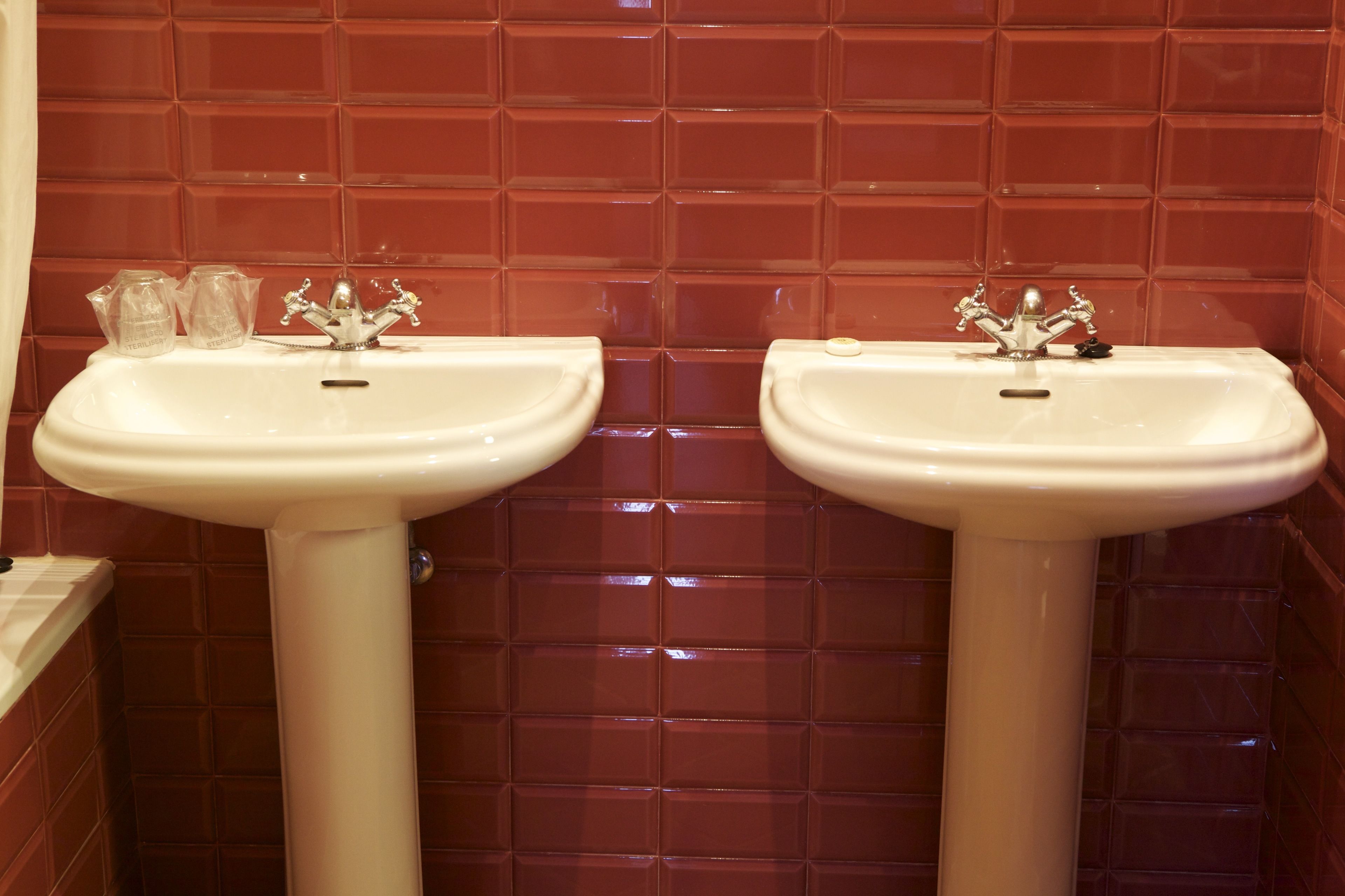 Een badkamer met twee witte wasbakken en rode betegelde wanden.
