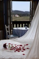A room with a bed, a table with a striped tablecloth, and a view of a landscape.