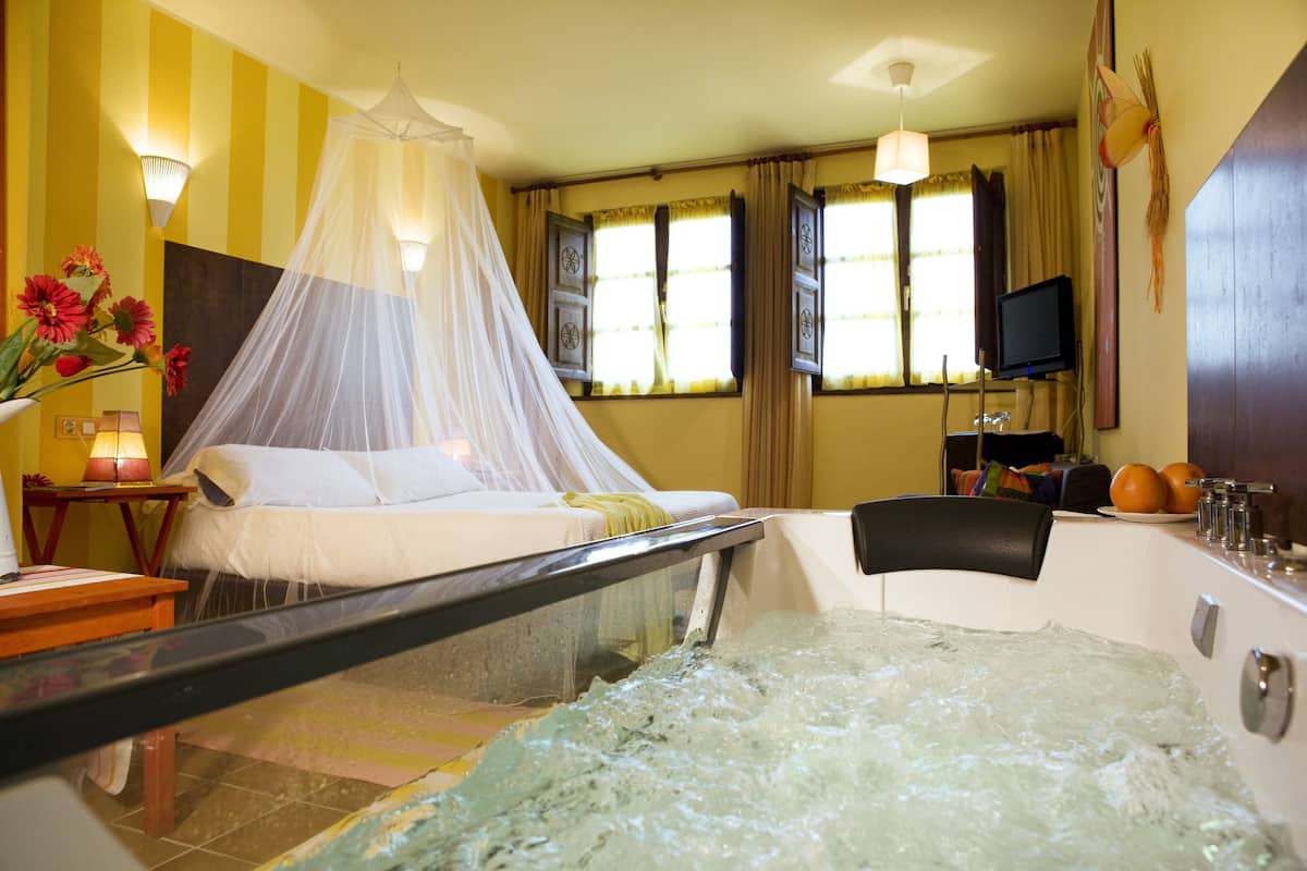 A hotel room with a bed, a bathtub, a TV, and a window with curtains.